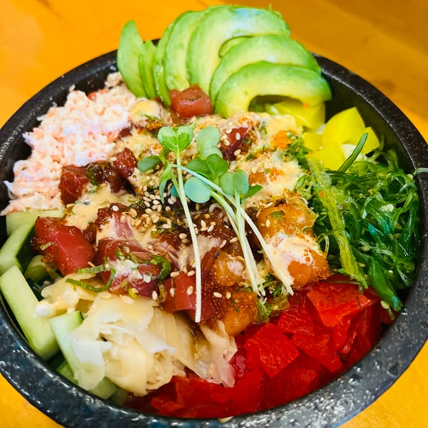 A vibrant poke bowl with tuna, avocado, crab salad, seaweed, pickled ginger, and microgreens.