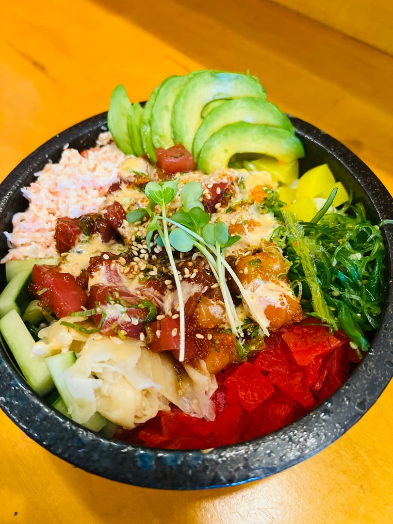 A vibrant poke bowl with tuna, avocado, crab salad, seaweed, pickled ginger, and microgreens.