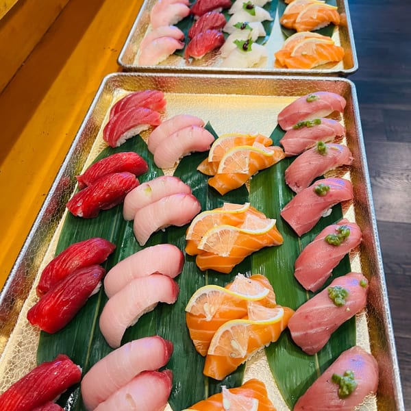 Two golden trays of assorted nigiri on bamboo leaves