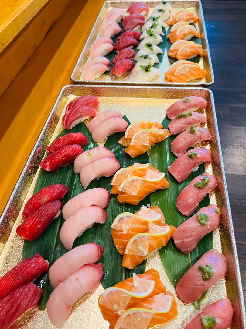 Two golden trays of assorted nigiri on bamboo leaves