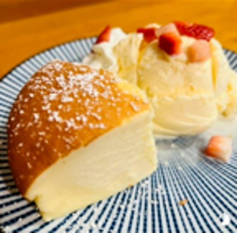 Fluffy cheesecake slice with vanilla ice cream, whipped cream, and strawberries on a striped plate.