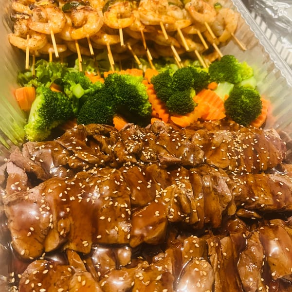 Catering tray of chicken and beef teriyaki with shrimp skewers and steamed vegetables