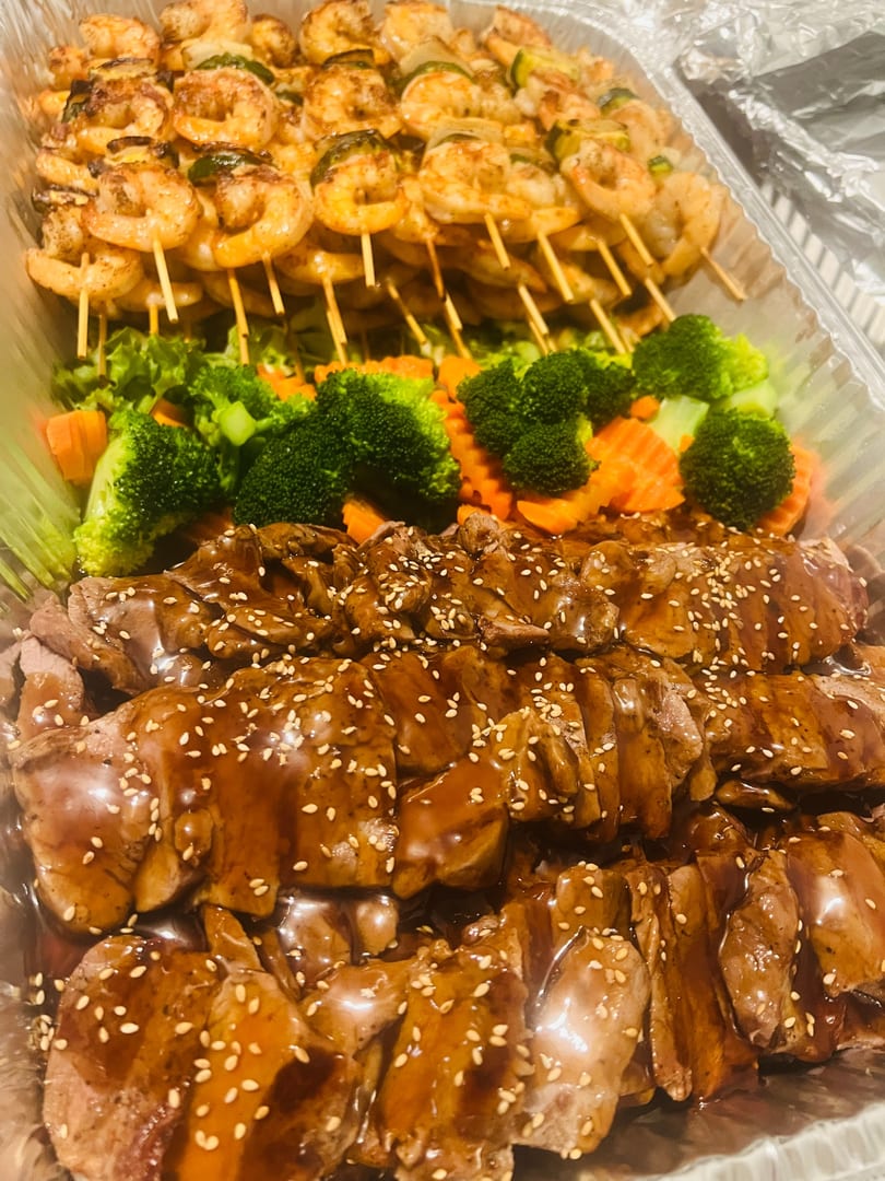 Catering tray of chicken and beef teriyaki with shrimp skewers and steamed vegetables