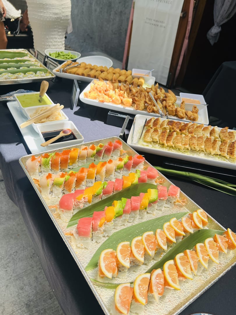 A buffet table laden with sushi rolls, gyoza, spring rolls, and other appetizers.