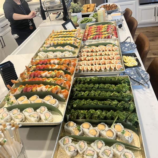 A large buffet spread of various sushi rolls, seaweed salad, and other appetizers on a white counter.