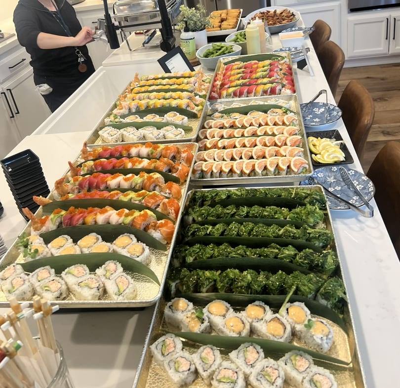 A large buffet spread of various sushi rolls, seaweed salad, and other appetizers on a white counter.