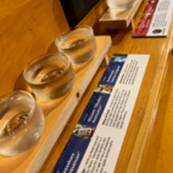 Three glasses of sake on wooden trays with tasting notes on a wooden bar.