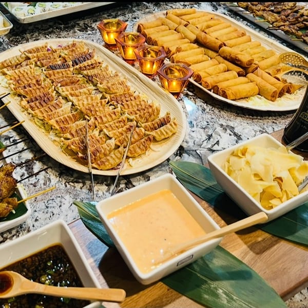Chicken skewers, gyoza, spring rolls, and dipping sauces on a catering table