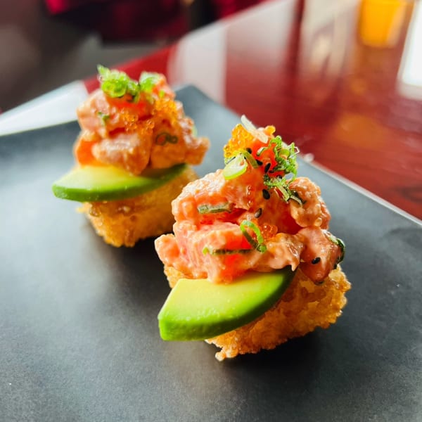 Two crispy rice bites with salmon tartare, avocado, green onions, and orange roe.