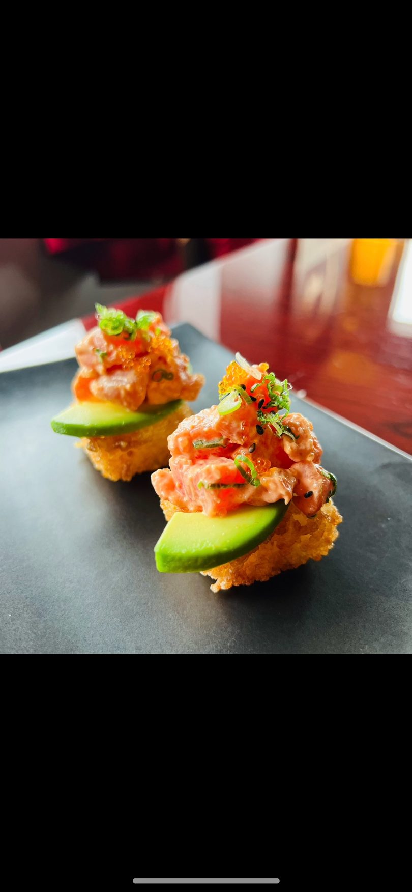 Two crispy rice bites with salmon tartare, avocado, green onions, and orange roe.