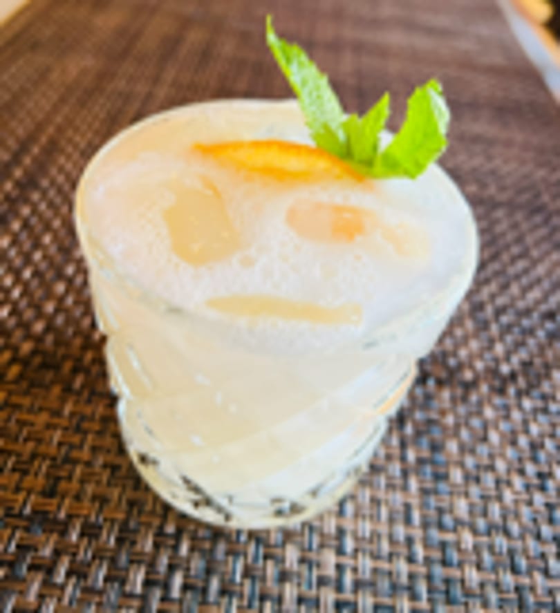 Foamy cocktail garnished with mint and orange peel on a dark placemat.