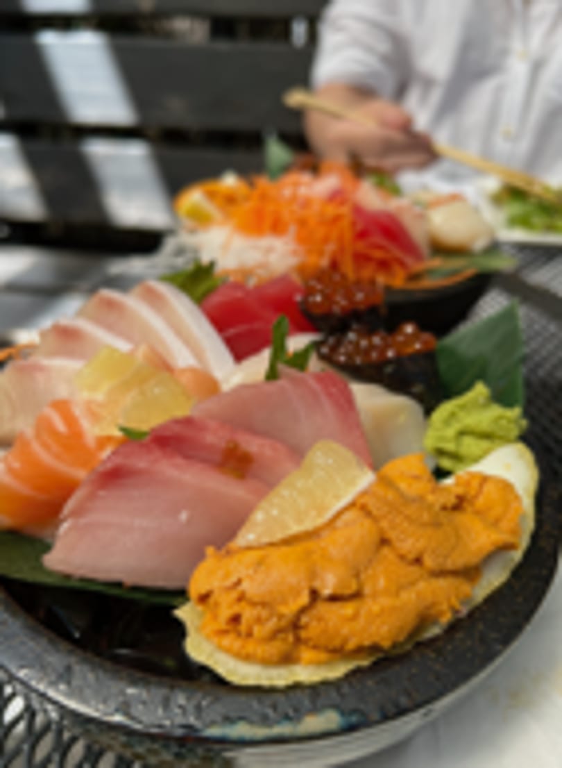 Close-up of a vibrant sashimi and uni platter with a person dining in the background.