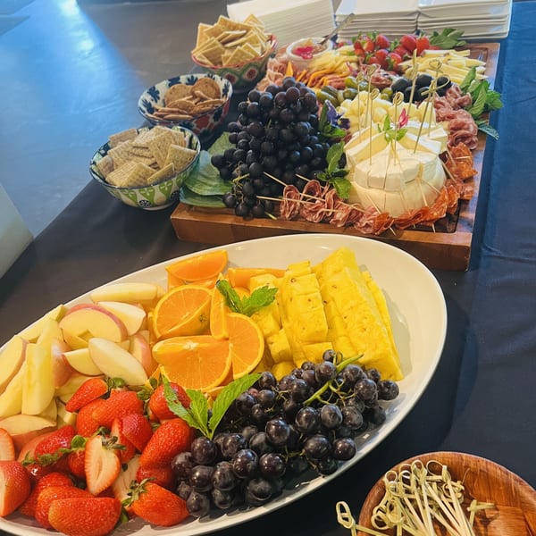 A vibrant charcuterie board with cheeses, meats, grapes, and crackers, alongside a fresh fruit platter.