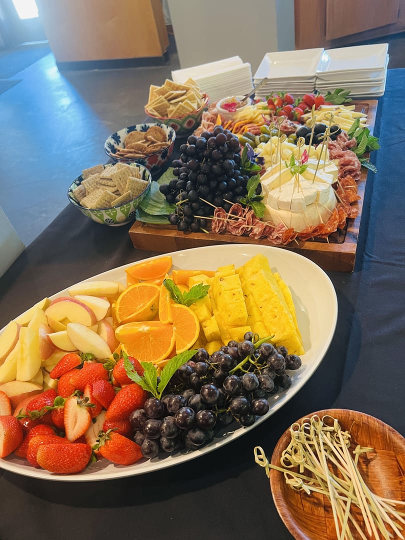 A vibrant charcuterie board with cheeses, meats, grapes, and crackers, alongside a fresh fruit platter.