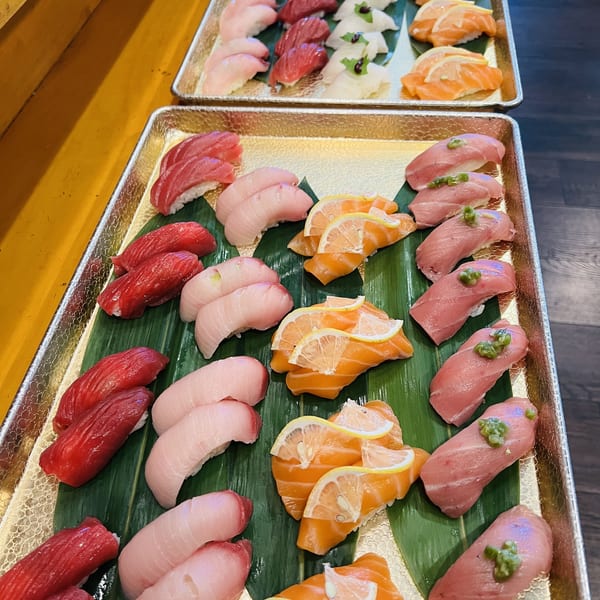 Two gold trays filled with rows of various sushi, including tuna, salmon, and white fish.