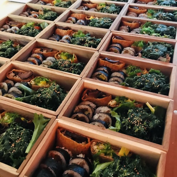 Rows of wooden bento boxes filled with sushi rolls, green vegetables, and inari pockets.
