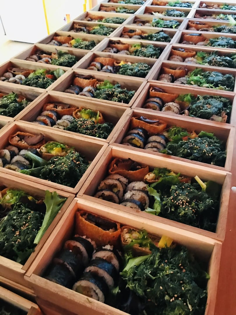 Rows of wooden bento boxes filled with sushi rolls, green vegetables, and inari pockets.