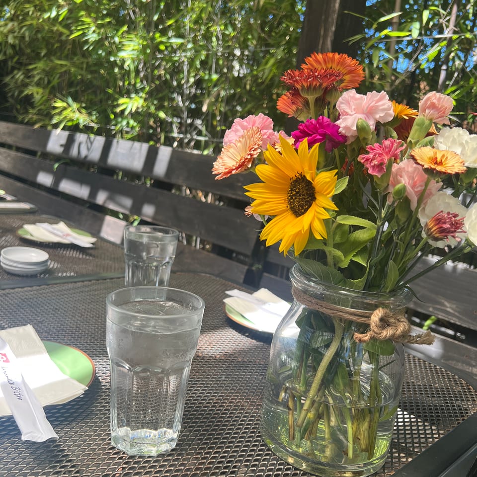 A vibrant flower bouquet on an outdoor patio table with water glasses and lush green bamboo.